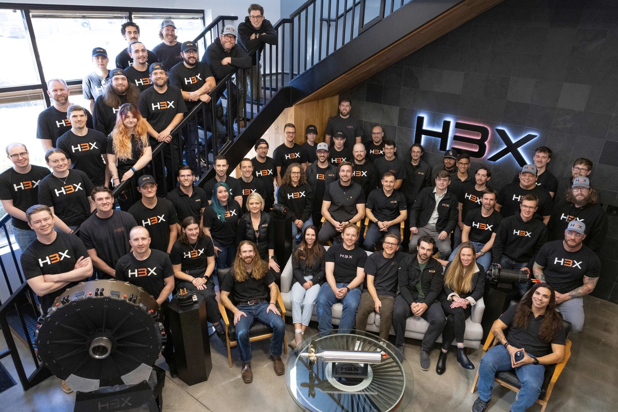The H3X team posed on and around the office staircase beneath the illuminated H3X logo, with motor hardware displayed in front